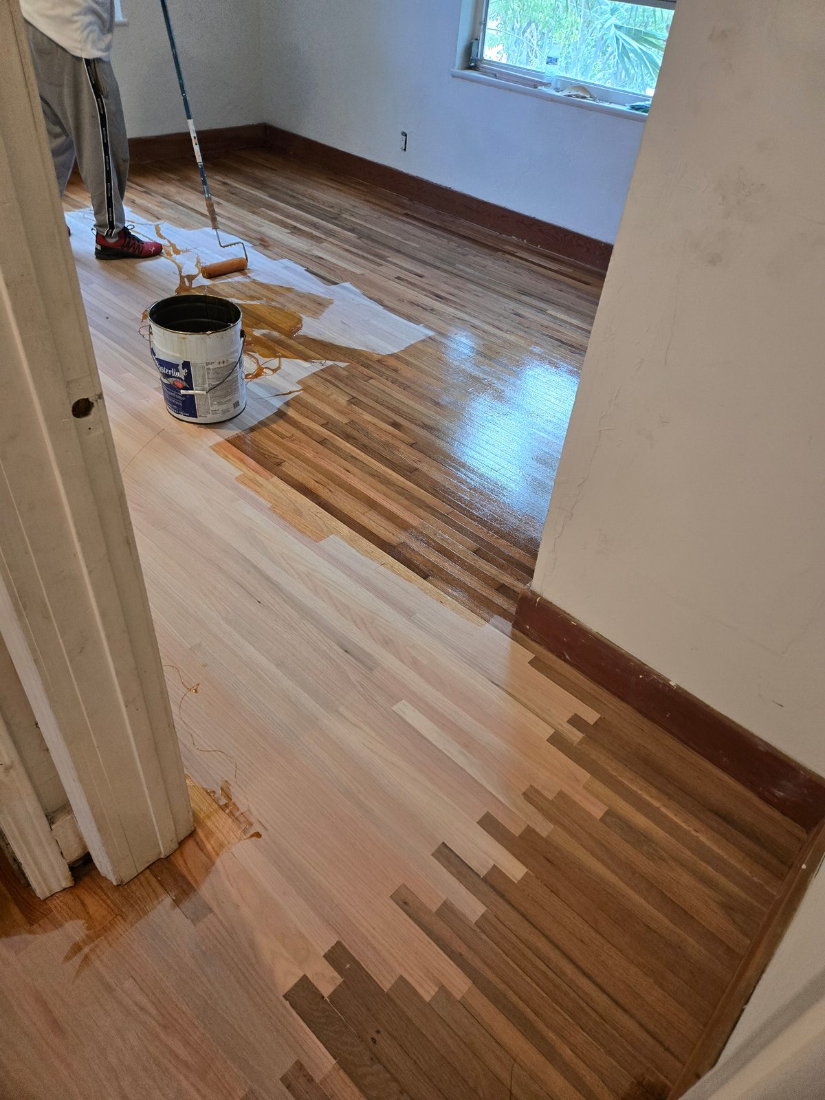 Worker applying finish with a roller to partially stained hardwood flooring in Hollywood, FL